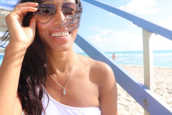 woman on beach  sitting on lifeguard tower steps wearing the pill pendant from the wandering jewel