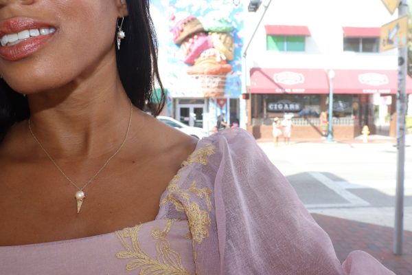 black woman standing in front of an ice cream shop wearing a renaissance pink princess top  with a pearl ice cream pendant and matching earrings from the wandering jewel