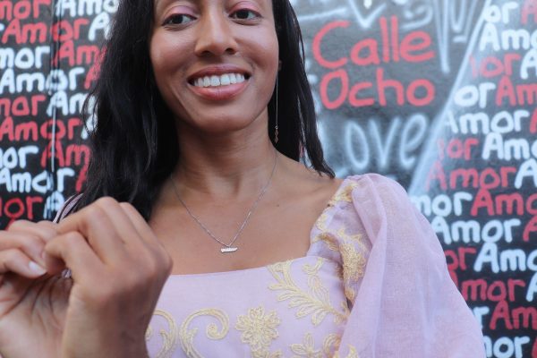 woman standing in front of a graffiti heart wall and making a heart shape with her hands and wearing the 7 diamonds heartburst necklace from the wandering jewel