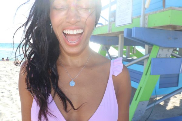 woman on beach in purple bikini smiling huge with her eyes closed wearing the yahweh coin pendant from The Wandering Jewel