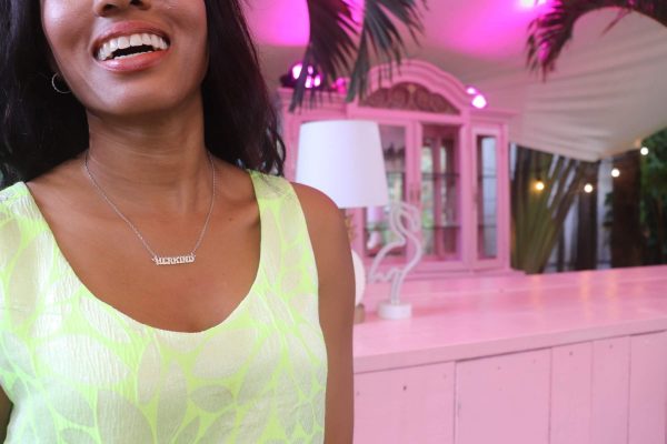 woman smiling in pink room and wearing a a neon yellow dress and the herkind nameplate necklace from the wandering jewel