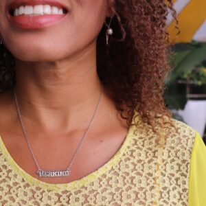 woman with brown curly hair smiling and wearing the herkind nameplate necklace from the wandering jewel