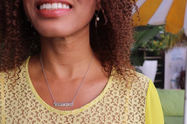 woman with brown curly hair smiling and wearing the herkind nameplate necklace from the wandering jewel