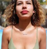 A beautiful woman at pool in green bikini looking up into the sky  wearing a nameplate necklace that says shekind