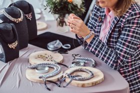a woman repairing a necklace that is made of ribbon and gems
