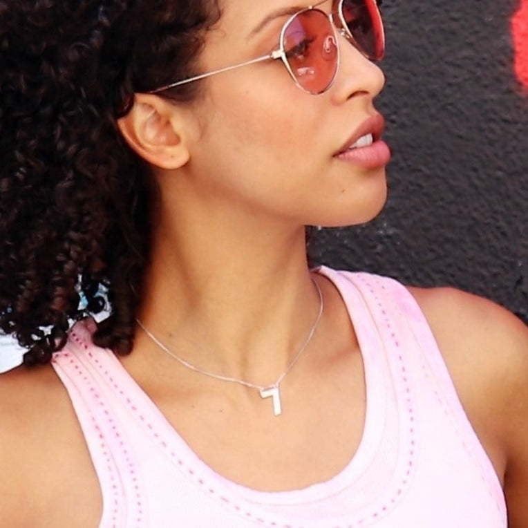 woman with sunglasses with a pink tank top wearing a diamond number  seven necklace from the wandering jewel