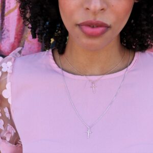 woman in pink dress wearing two crosses one silver and one rose gold from the wandering jewel