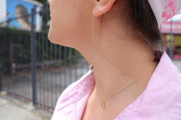 brunette woman in pink top looking to her right side wearing dice earrings and matching dice pendant from the wandering jewel