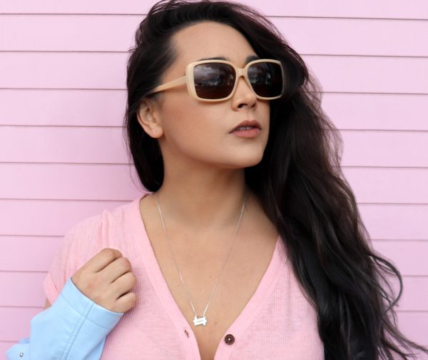 Woman with pink shirt and sunglasses on in front of a pink  house wearing a Double seven necklace from the wandering jewel