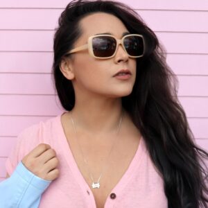 Woman with pink shirt and sunglasses on in front of a pink  house wearing a Double seven necklace from the wandering jewel