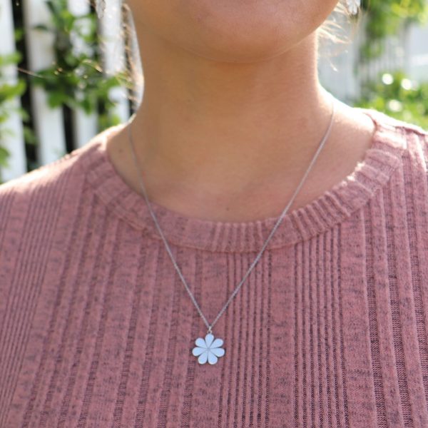 woman in pink shirt standing in front of a white picket fence wearing flower pendant necklace from the wandering jewel