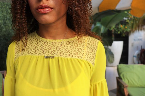 black woman at pool in a yellow dress at wearing a mutha mother necklace from the wandering jewel