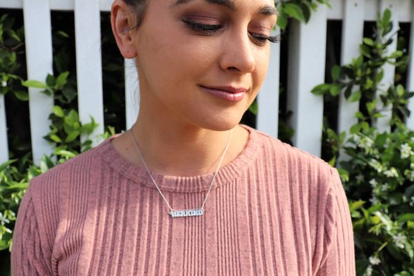 woman in pink shirt in front of white fence wearing herkind necklace from the wandering jewel