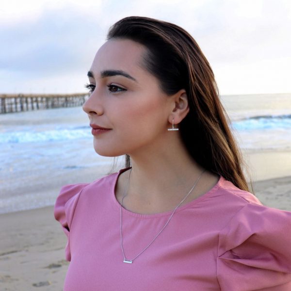 woman in pink dress on the beach wearing diamond bar earrings from the wandering jewel