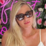 blonde woman smiling in sunglasses wearing gold pearl necklace from the wandering jewel