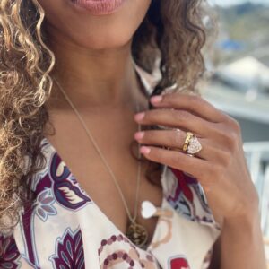 Black woman in floral dress on beach showing off her large puff heart diamond ring from the wandering jewel