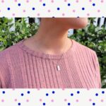 woman in pink shirt in front of white picket fence in garden wearing a tiny pill  shaped pendant necklace from the wandering jewel
