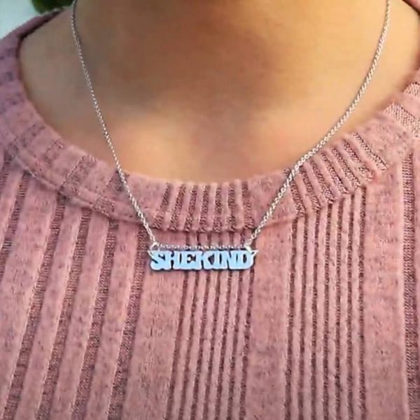 woman in pink shirt wearing a nameplate necklace that says shekind