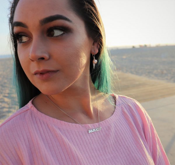 white woman with blue hair and pink t shirt on beach wearing journey nameplate necklace