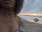 A woman on the beach in a multicolor bikini wearing a journey nameplate necklace