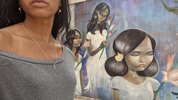 woman in gray top in front of mural wearing two 7 diamond crosses from the wandering jewel