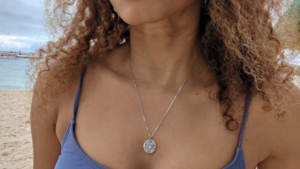 woman purple bikini with long brown curly hair wearing the 7 diamond star of david coin pendant by the wandering jewel