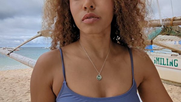 woman in purple bikini on beach wearing yahweh coin pendant necklace from the wandering jewel