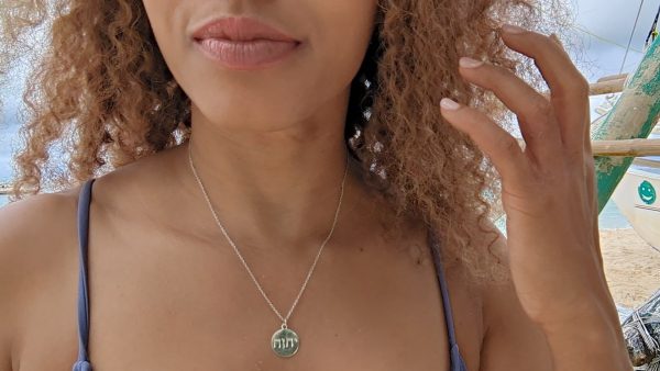 woman in purple swimsuit on beach with fishing boat in the background wearing Jehovah coin pendant  from the wandering jewel