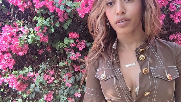 woman in brown dress in front of pink flowers wearing the groovy mutha necklace from the wandering jewel