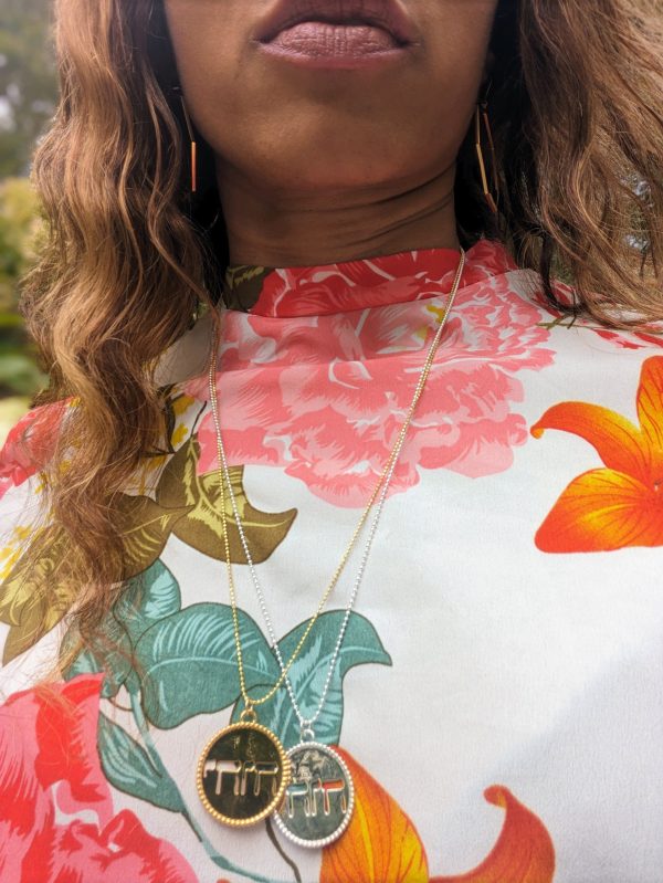 black woman in floral dress in garden wearing the Jehovah cutout coin from the wandering jewel