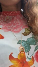 black woman in floral dress in garden wearing the Jehovah cutout coin from the wandering jewel