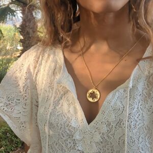 black woman in white dress in garden wearing the Rose gold star of David pendant necklace coin from the wandering jewel