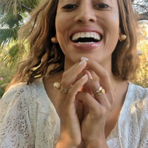black woman with straight hair laughing  in garden in a white dress and wearing the gold septagon disengagement ring from the wandering jewel