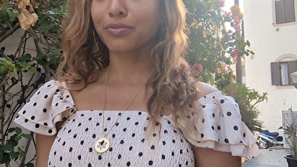 black woman wearing a polka dot dress on a European street and wearing the Rose gold star of David pendant necklace coin from the wandering jewel