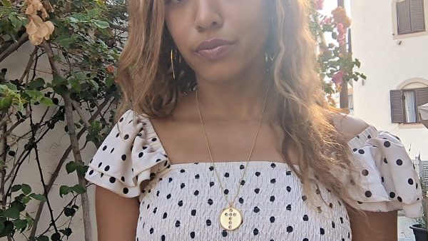 black woman in polka dot dress in Greek island wearing the cross cutout coin from the wandering jewel