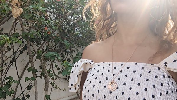 black woman in polka dot dress on a Greek island wearing the Rose gold star of David pendant necklace coin from the wandering jewel