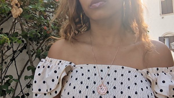 black woman in polka dot dress on a Greek island wearing the Rose gold star of David pendant necklace coin from the wandering jewel