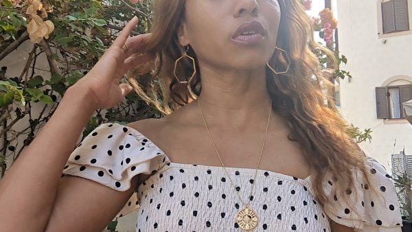 black woman in European village in polka dot dress wearing Large gold hoop diamond earrings septagon shaped from the wandering jewel