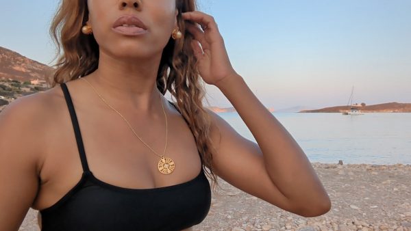 black woman on Greek beach in black bikini wearing large gold South sea pearl diamond earring studs from the wandering jewel