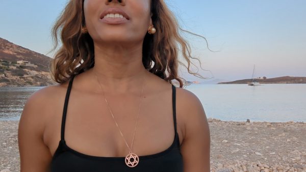 black woman in black bikini on Greek beach wearing the Rose gold star of David pendant necklace coin from the wandering jewel