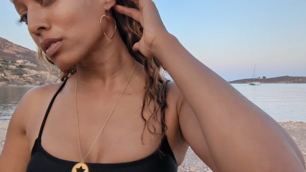 woman in black bikini on beach wearing large hoop earrings shaped like a heart form the wandering jewel