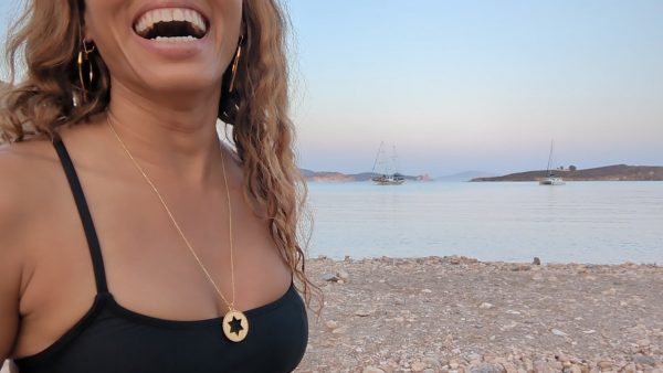 smiling black woman in black bikini on Greek beach wearing the Rose gold star of David pendant necklace coin from the wandering jewel