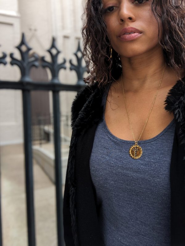 black woman with curly hair in blue dress and fur necklace wearing the 7 diamond Semper Fi Coin Pendant necklace from the wandering jewel