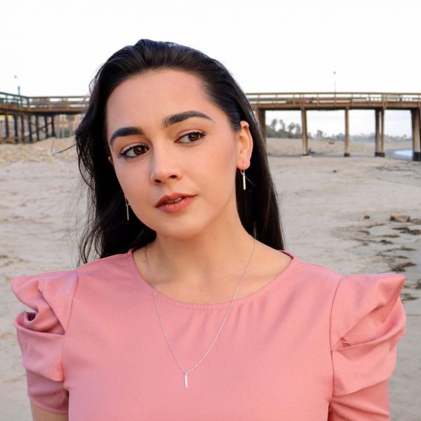 woman waiting on beach in a pink dress wearing diamond pillar necklace from the wandering jewel