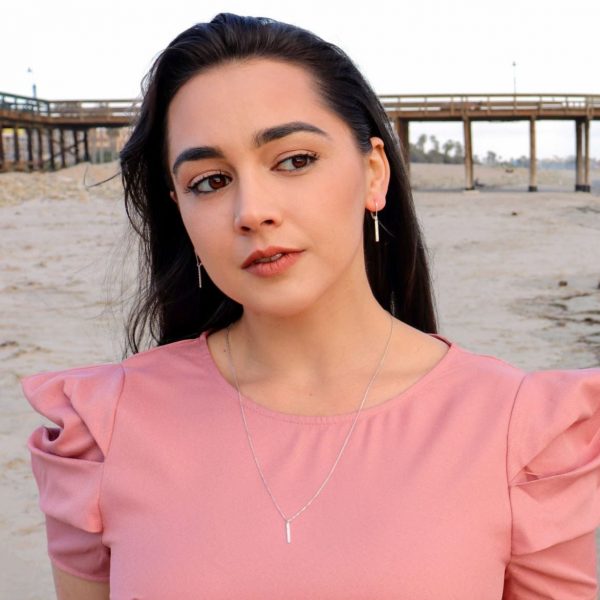 woman at beach in a pink dress wearing pillar bar diamond earrings from the wandering jewel