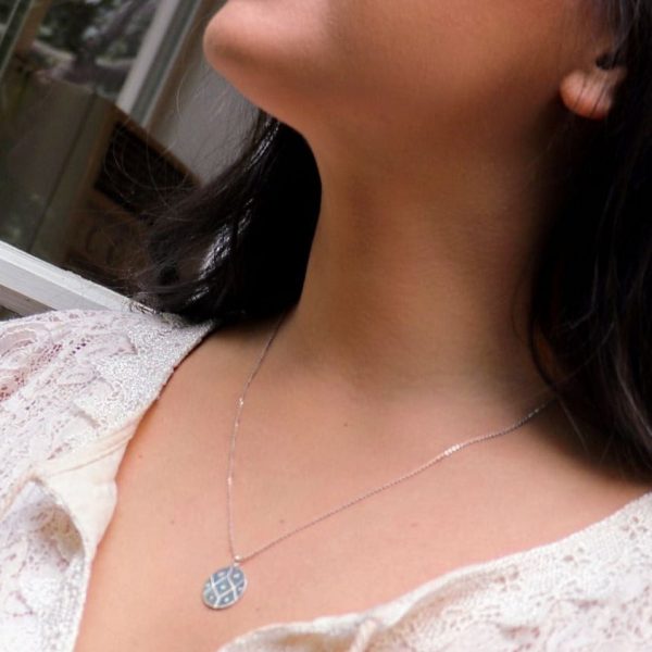 woman in a white dress in front of a window wearing a diamond coin necklace from the wandering jewel