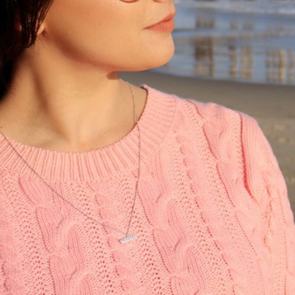 woman in pink sweater on the beach wearing seven hearts diamond pendant necklace from the wandering jewel