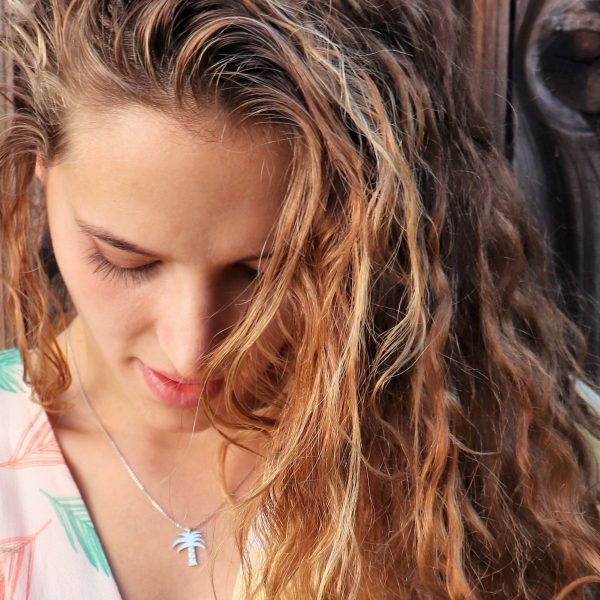 blonde Woman looking down and wearing a tiny Palm Tree necklace from the wandering jewel