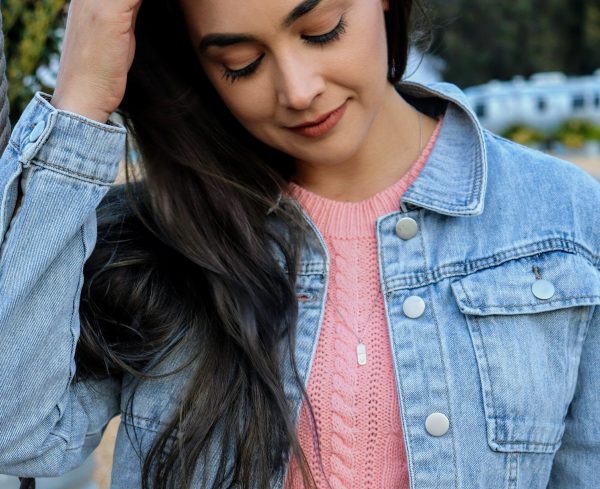 woman in pink sweater and light blue denim jacket wearing a diamond pill necklace from the wandering jewel