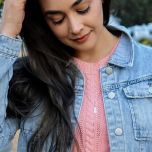 woman in pink sweater and light blue denim jacket wearing a diamond pill necklace from the wandering jewel